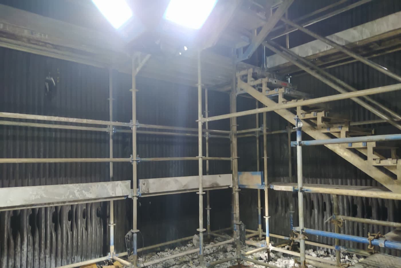 Interior de espaço confinado com andaimes montados e iluminação no topo durante a parada de manutenção